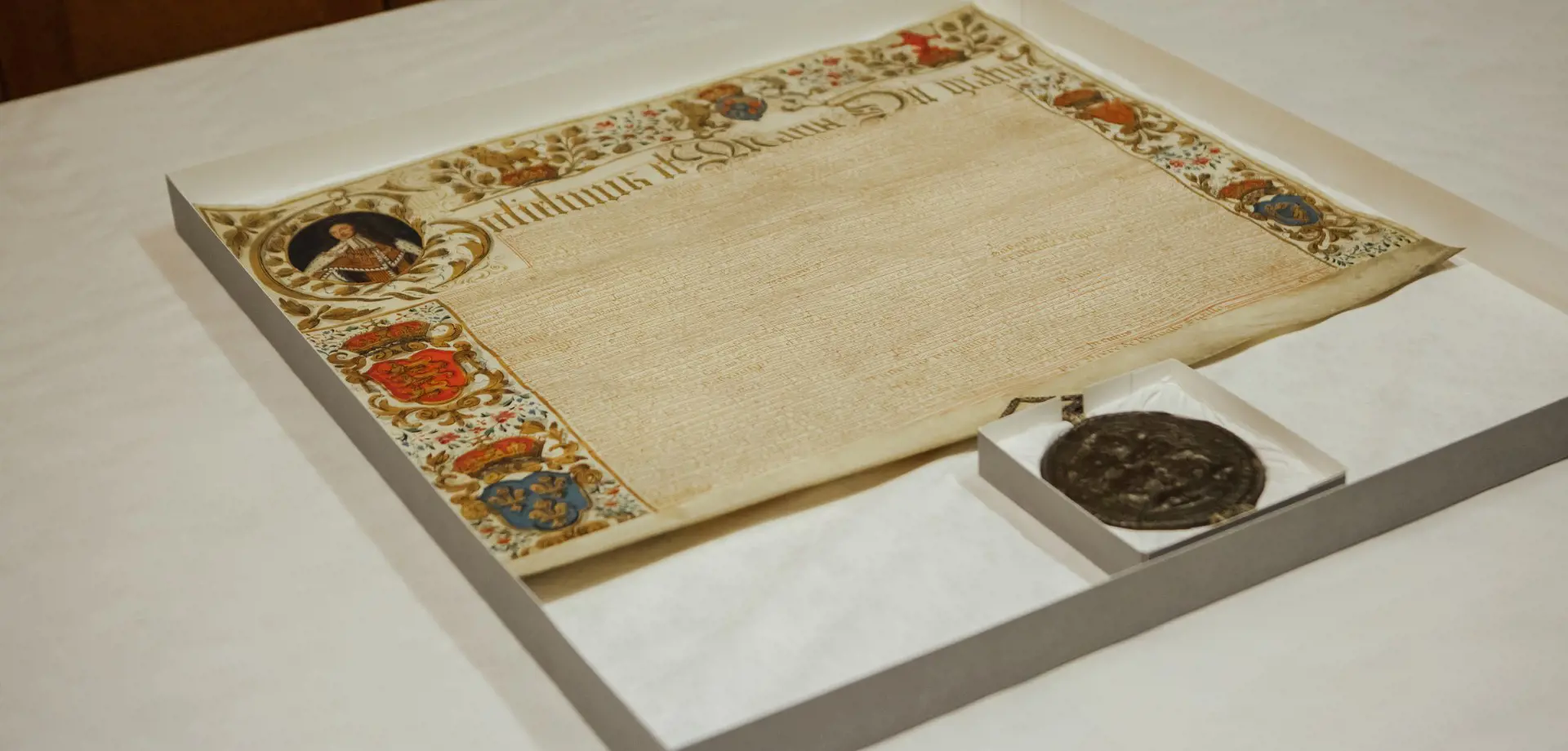 Large parchment with brightly coloured illustrations around the edges, including a portrait of William, dense writing and a large dark red round seal hanging from the bottom
