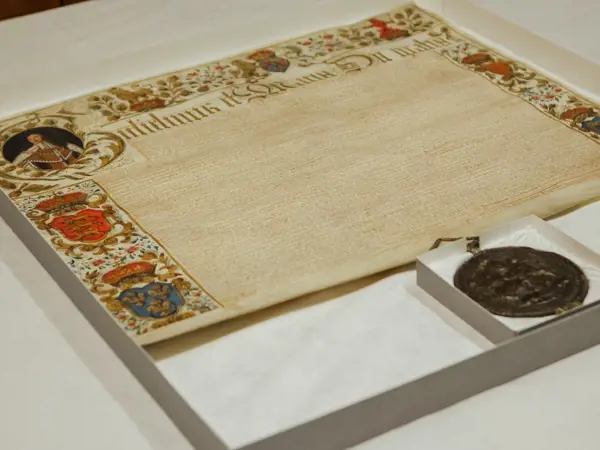 Large parchment with brightly coloured illustrations around the edges, including a portrait of William, dense writing and a large dark red round seal hanging from the bottom