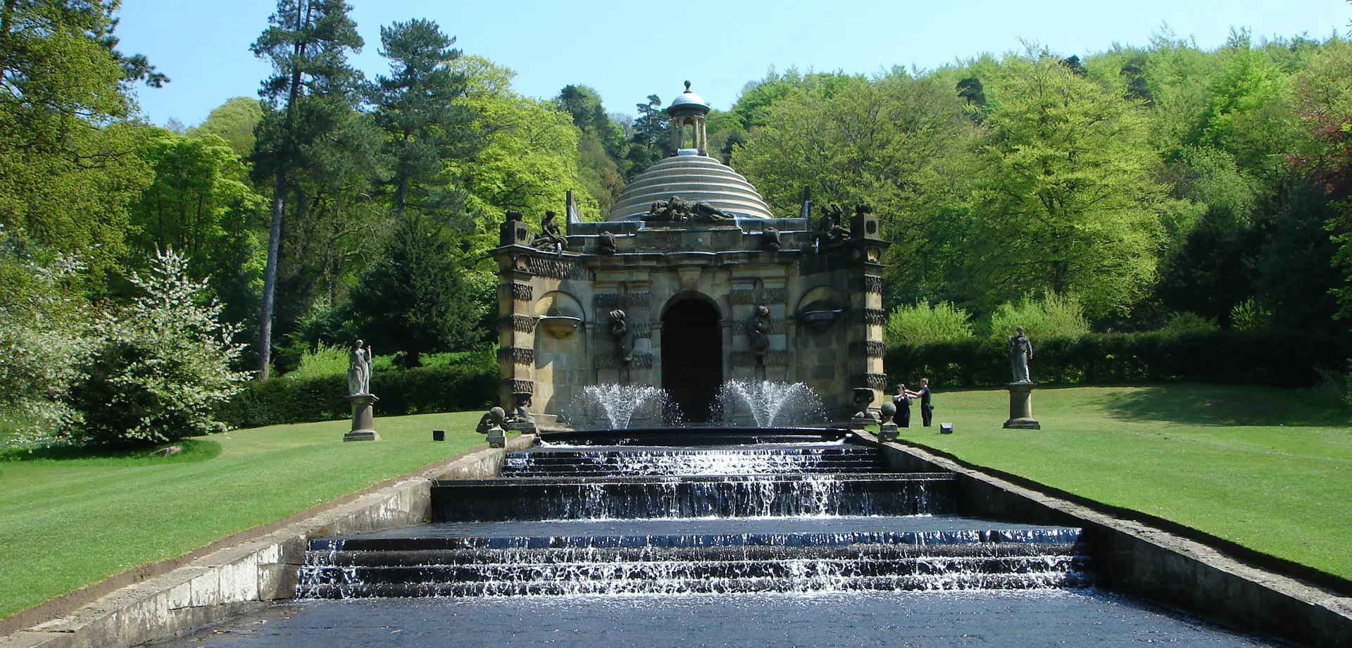 Early 18th century stone temple with carvings from which water descending down a series of stone steps, grass either side and trees behind it